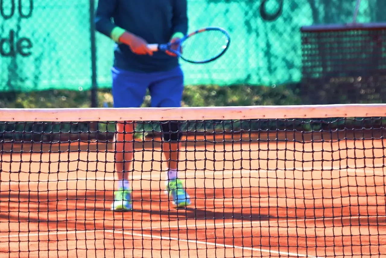 Tennisspiller bag nettet på grusbane